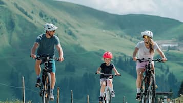 Three people riding bicycles on a road with a mountainous landscape in the background.