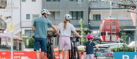 Een groep mensen met fietsen, een rood voertuig en een gebouw met een bord waarop staat 'AUDI QUATTRO parkeer hier'.