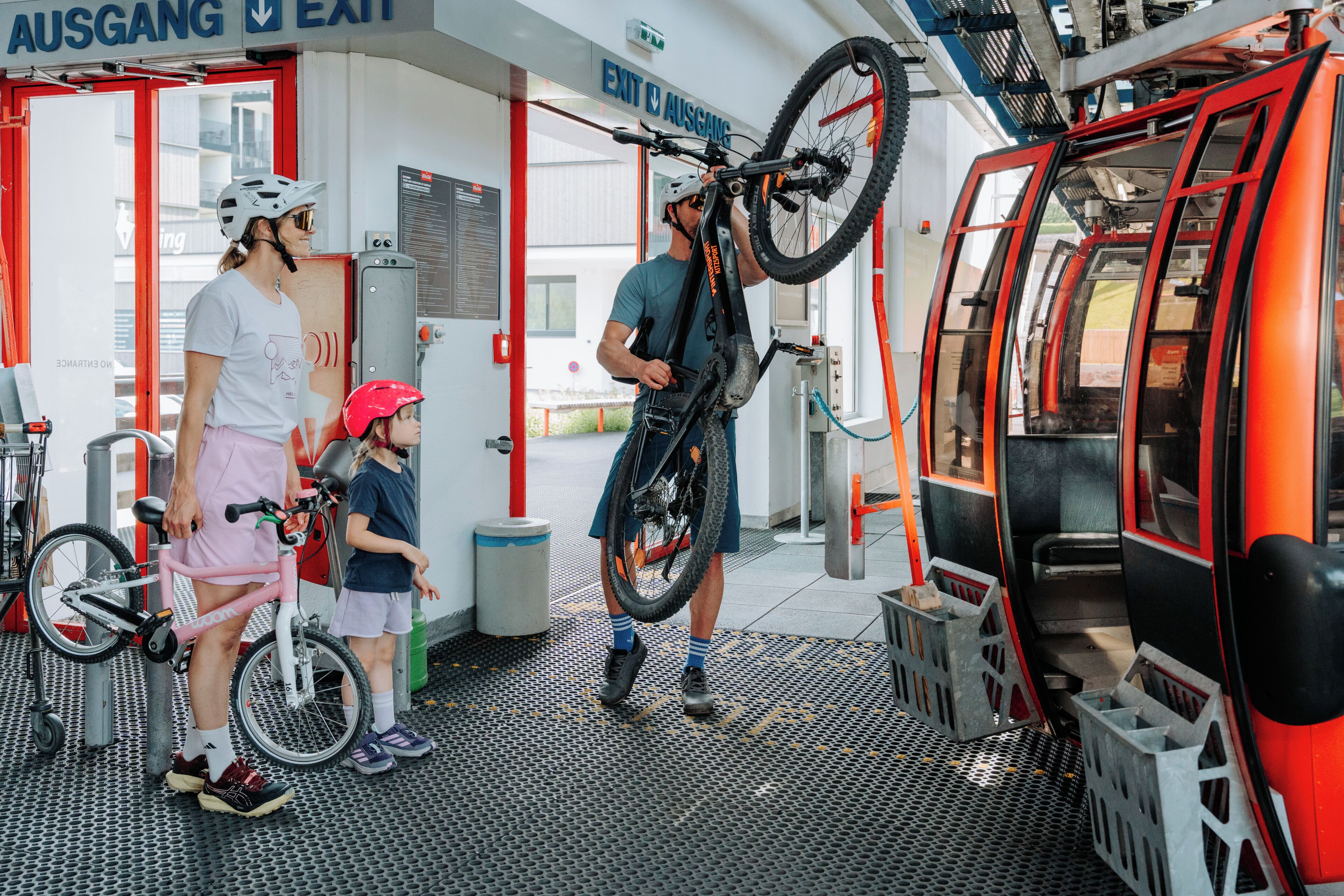 En cykeluthyrningsstation med en röd och vit byggnad, en skylt med texten ”UTGÅNG”, och en person som håller i en cykel.