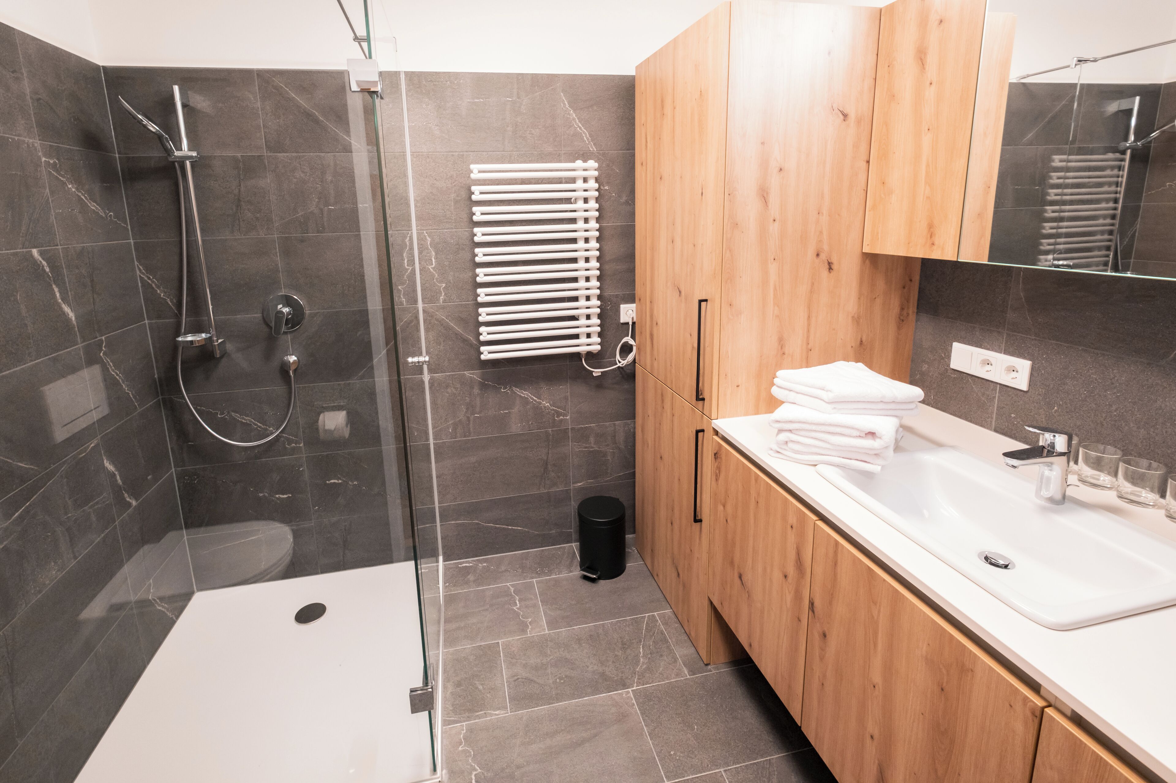 A modern bathroom with a glass-enclosed shower, a white sink, and wooden cabinets.