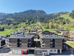 A modern hotel with a self-check-in kiosk, surrounded by mountainous terrain and lush greenery. - KitzSki Living (Kitzbühel)