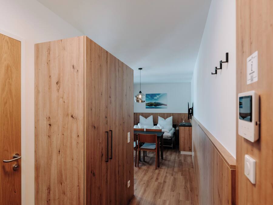 Un pasillo con suelo de madera, un comedor con mesa y sillas, y una zona de cocina con estufa y encimera.