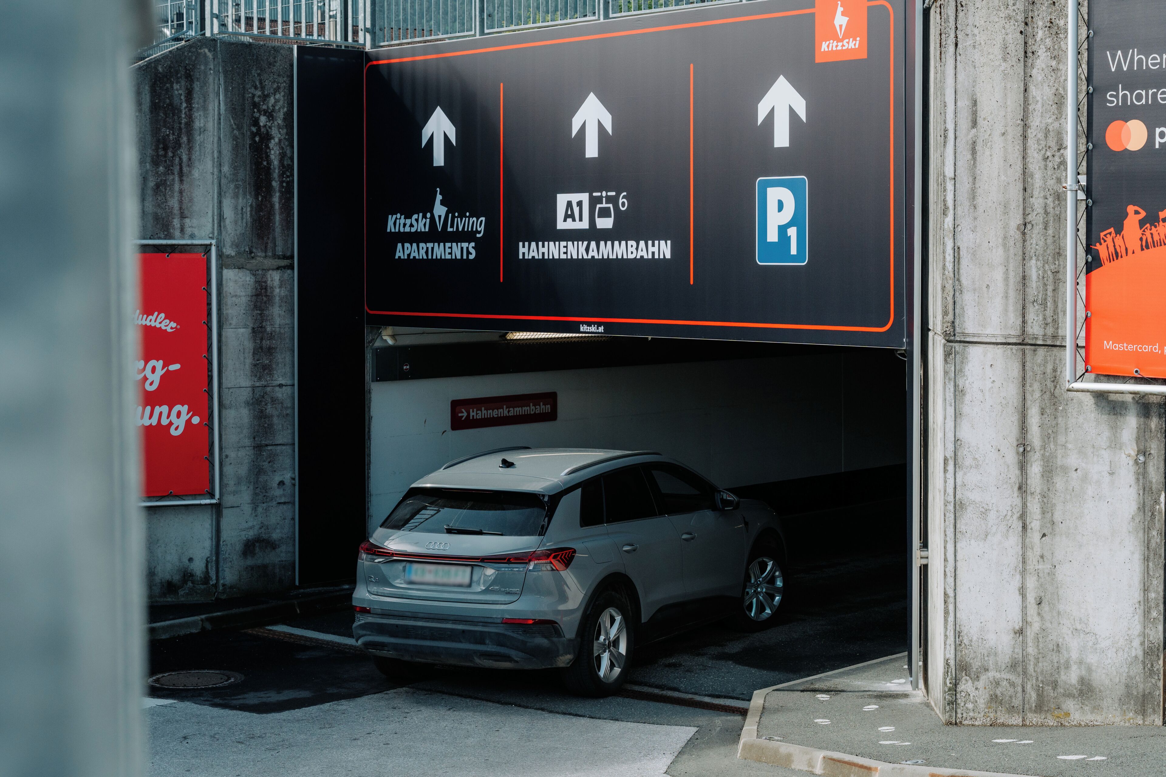 Un auto entra a un estacionamiento con indicaciones que señalan hacia apartamentos y una zona de estacionamiento.