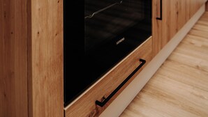 A modern kitchen with wooden cabinets, a black oven, and a microwave above it. - KitzSki Living (Kitzbühel)
