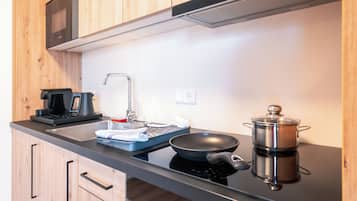 Een moderne keuken met houten kastjes, een zwart aanrecht, een magnetron, een koffiezetapparaat, een spoelbak en een kookplaat met een pan.