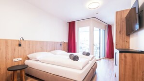 A modern hotel room with a bed, a small table, a TV, and a view of the outside. - KitzSki Living (Kitzbühel)