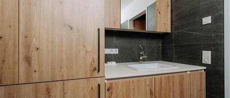 A modern bathroom with wooden cabinets, a white sink, and a dark tiled wall.