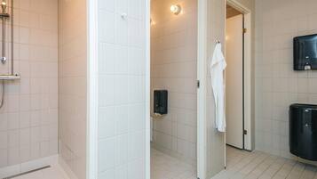 A bathroom with white tiles, a shower, a towel rack, and a soap dispenser.