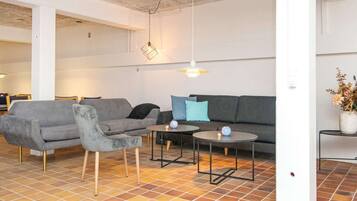 Una sala moderna con un sofá gris, un sillón a juego, dos mesitas redondas y una lámpara colgante.