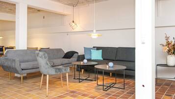 A modern living room with a grey sofa, a matching armchair, two small round tables, and a hanging light fixture.