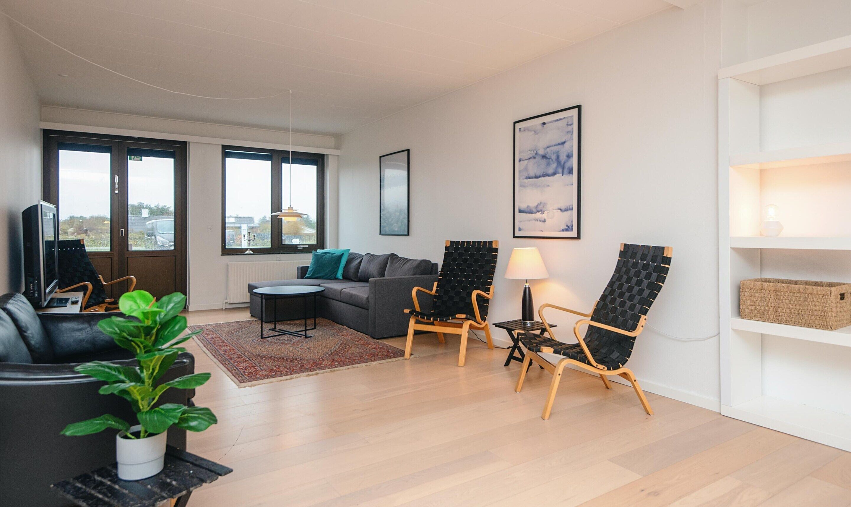 A modern living room with a sofa, two armchairs, a coffee table, a TV, and a potted plant.