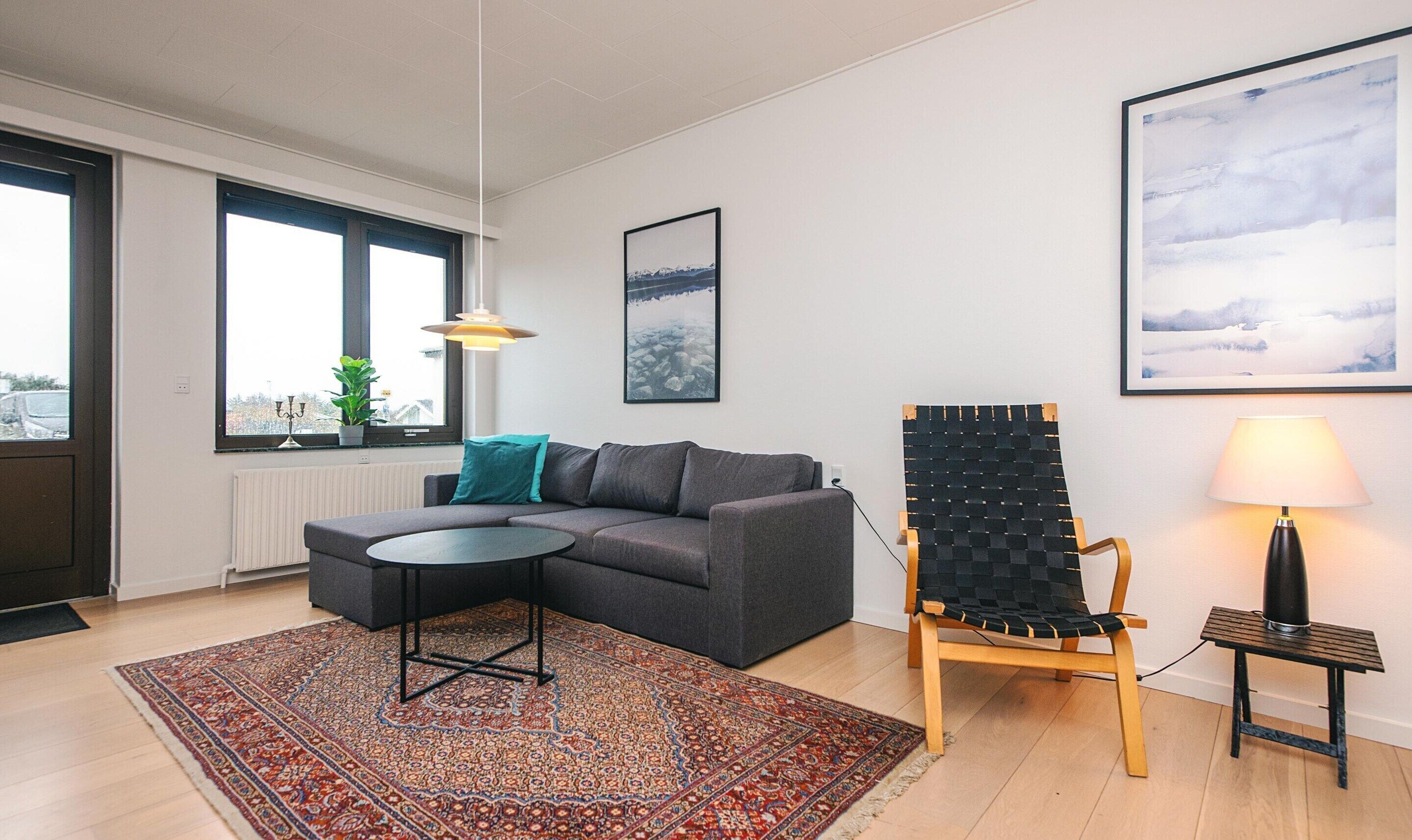 Ein modernes Wohnzimmer mit einem grauen Modulsessel, einem gemusterten Teppich, einem schwarzen Webstuhl-Sessel und einer Tischlampe.