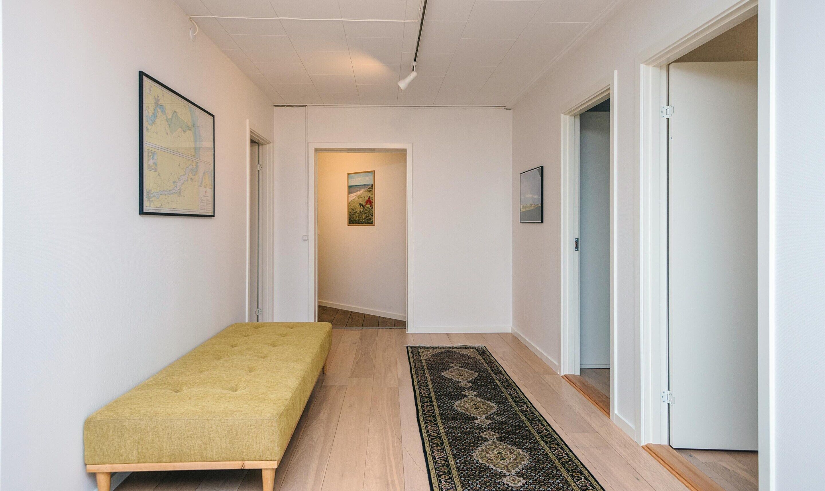 A narrow hallway with a bench, a rug, and a door leading to another room.