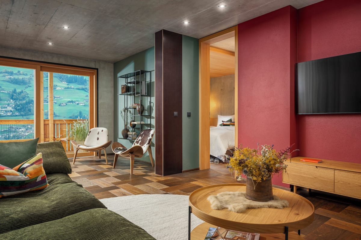 Uma sala de estar moderna com uma janela grande, um sofá, uma mesa de centro de madeira e uma televisão fixada na parede.