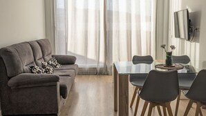 Un soggiorno moderno con un divano grigio, un tavolo da pranzo in vetro e una TV a parete.