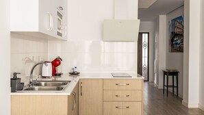 Una cucina moderna con lavello in acciaio inossidabile, bollitore rosso e piano di lavoro bianco. Si nota un mobiletto in legno con tre cassetti e un forno a microonde bianco fissato alla parete.