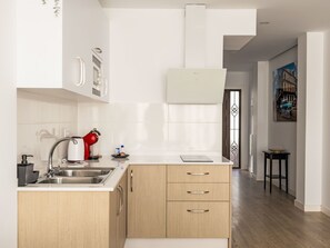 A modern kitchen with a stainless steel sink, a red kettle, and a white countertop. There is a wooden cabinet with three drawers and a white wall-mounted microwave. - Camino del Río - Caminito del Rey by Interhome (Ardales)
