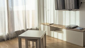 Una camera moderna con una scrivania in legno, una televisione a parete e una finestra con tende leggere.