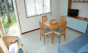 A room with a dining table, chairs, a sofa, a television, and a kitchen area. - Villa With Patio Near the Beach (Lignano Sabbiadoro)