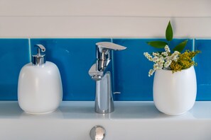 Ein Badezimmer mit einem weißen Waschbecken, einem chromfarbenen Wasserhahn und einer Vase mit Blumen.