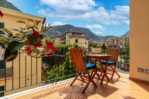 Ein Balkon mit Tisch und Stühlen, mit Blick auf eine Berglandschaft und eine Stadt.