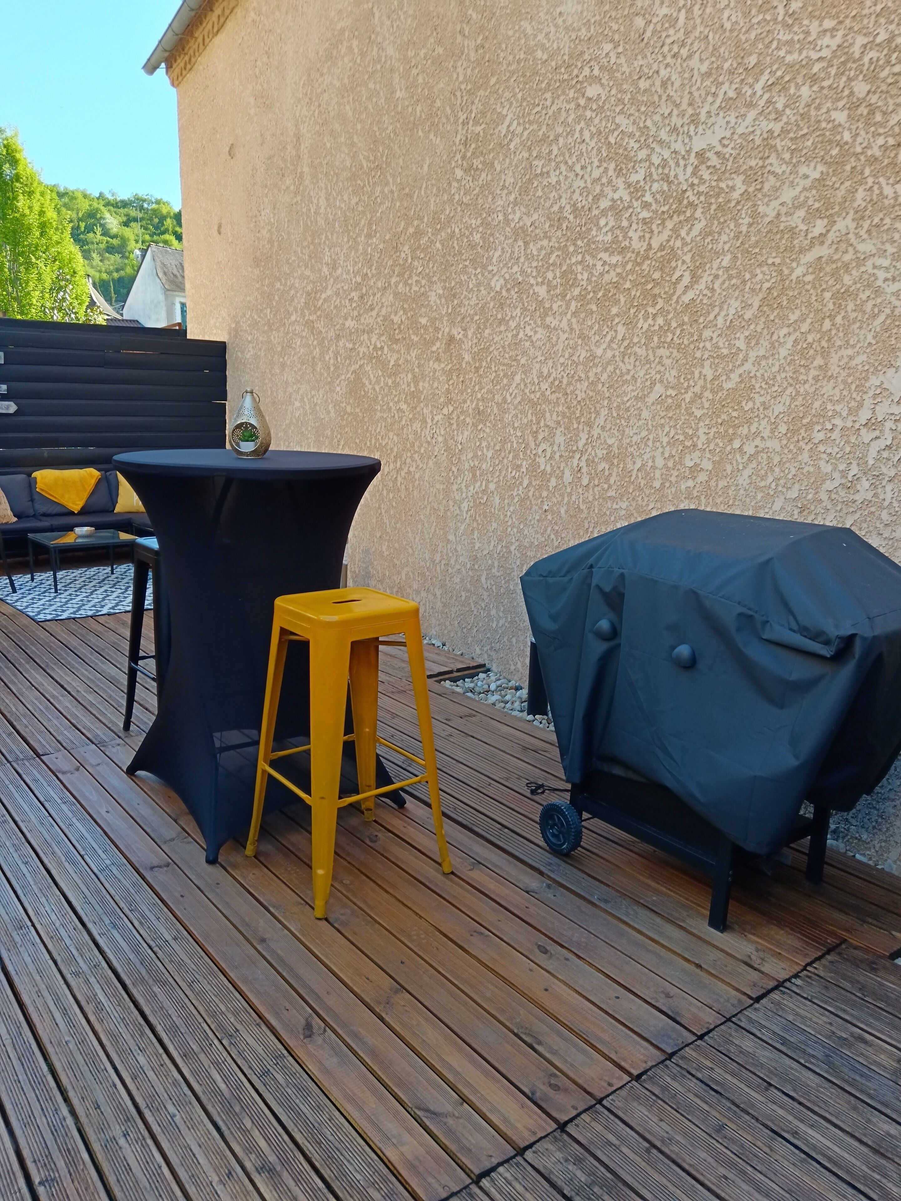 Een terras buiten met een zwarte tafel, een gele stoel en een barbecue.
