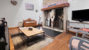 A living room with a stone fireplace, a wooden sofa, a coffee table, and a television. - Holiday Home “La Perle Rosée” with Private Terrace, and Wi-Fi (Azerat)