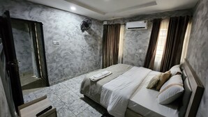 Una habitación de hotel con cama, mesita de noche, espejo, aire acondicionado y puerta.