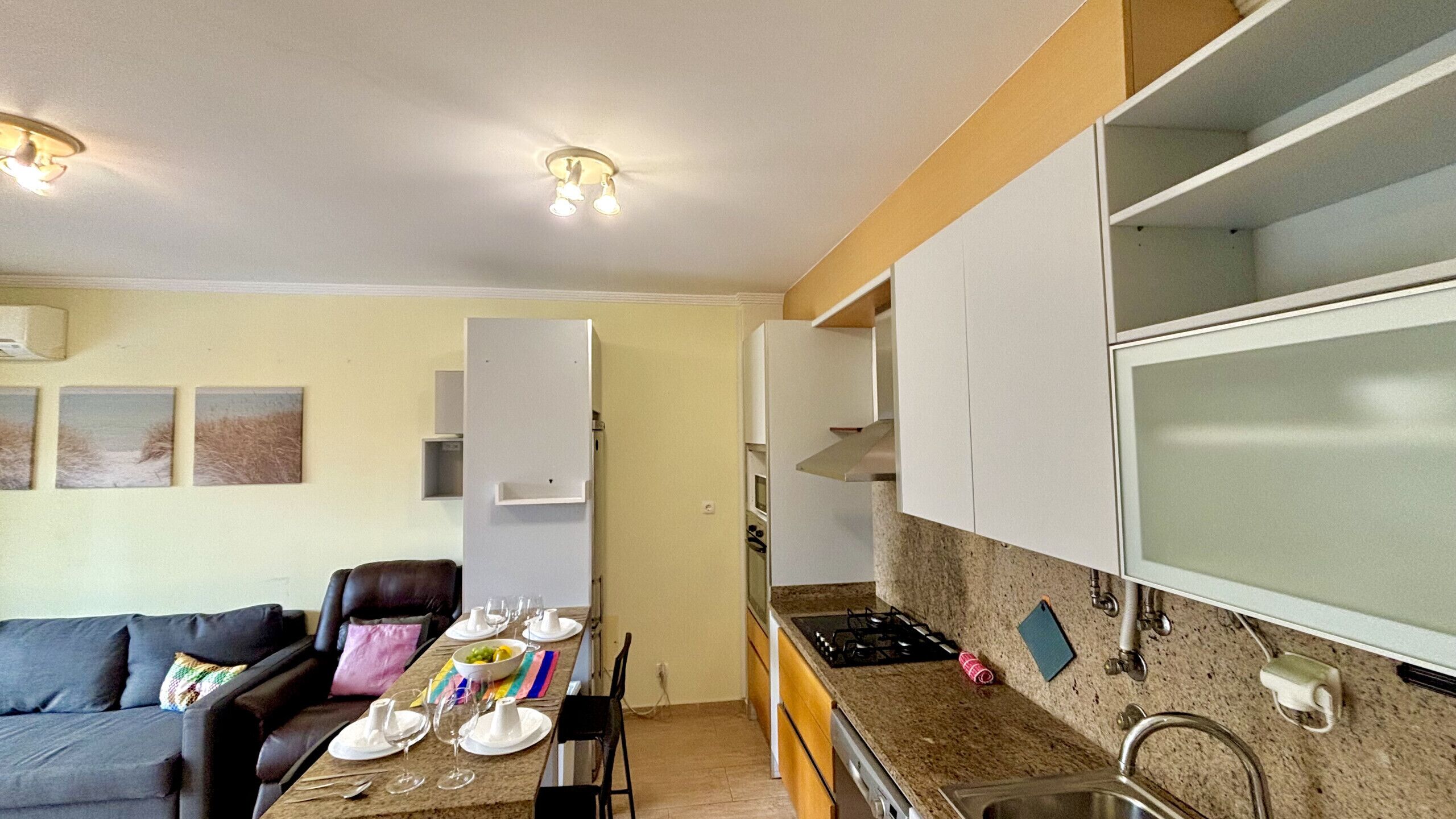 Un espace de vie compact comprenant un coin cuisine, un coin repas avec une table pour quatre personnes et un canapé.