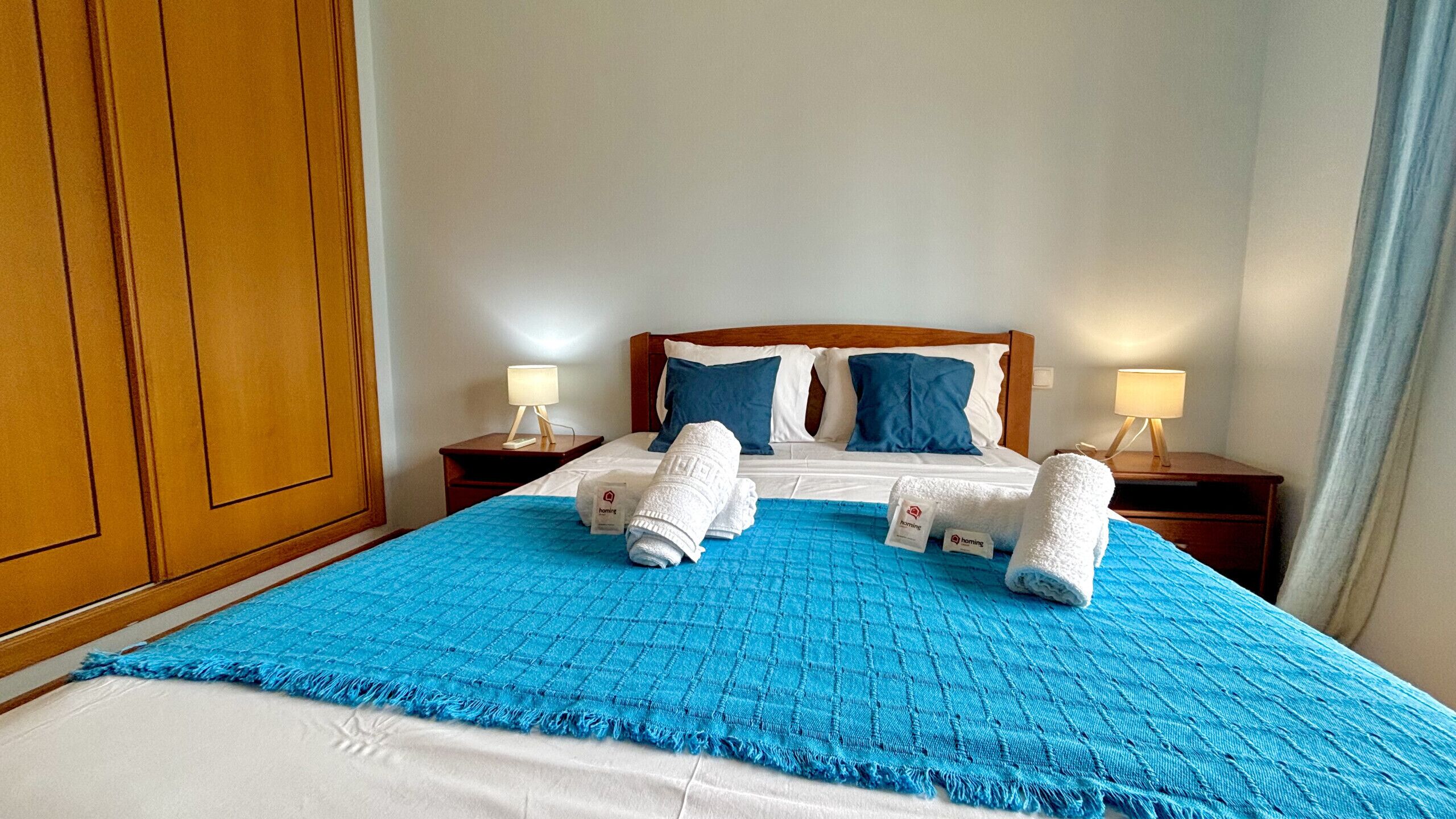 A hotel room with a bed, two nightstands, a blue bedspread, and two towels.