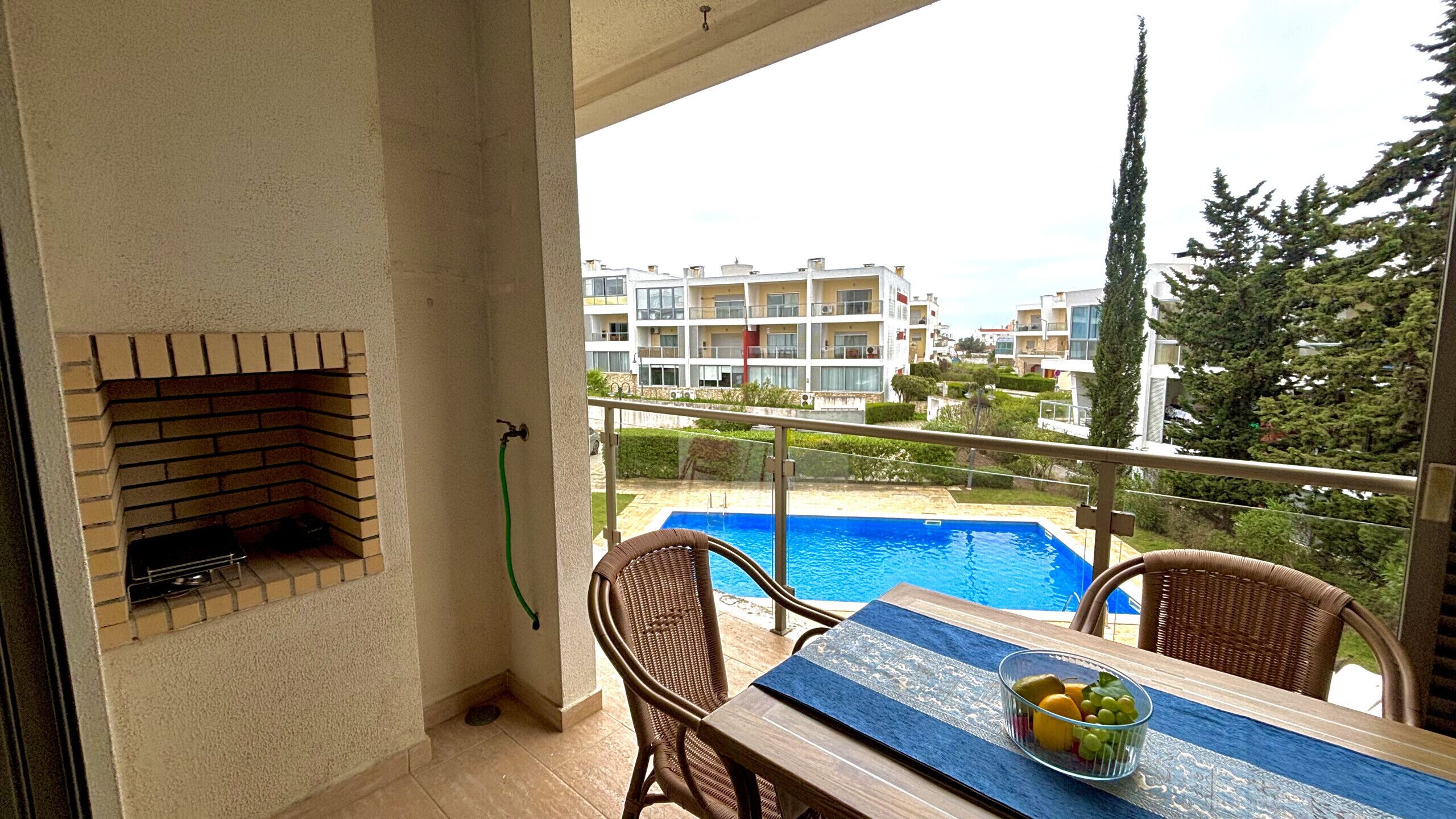 A balcony with a brick fireplace, a pool, and a table with fruit.