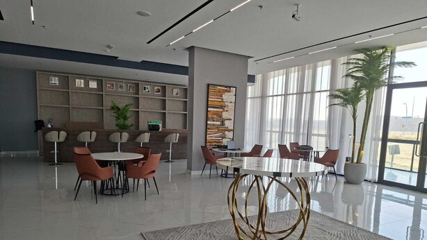 Een moderne vergaderruimte met een glazen tafel, meerdere stoelen, een decoratief vloerkleed en een groot raam met daglicht.