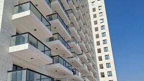 Een modern hoog gebouw met meerdere balkons en een rode looppad naar de ingang.