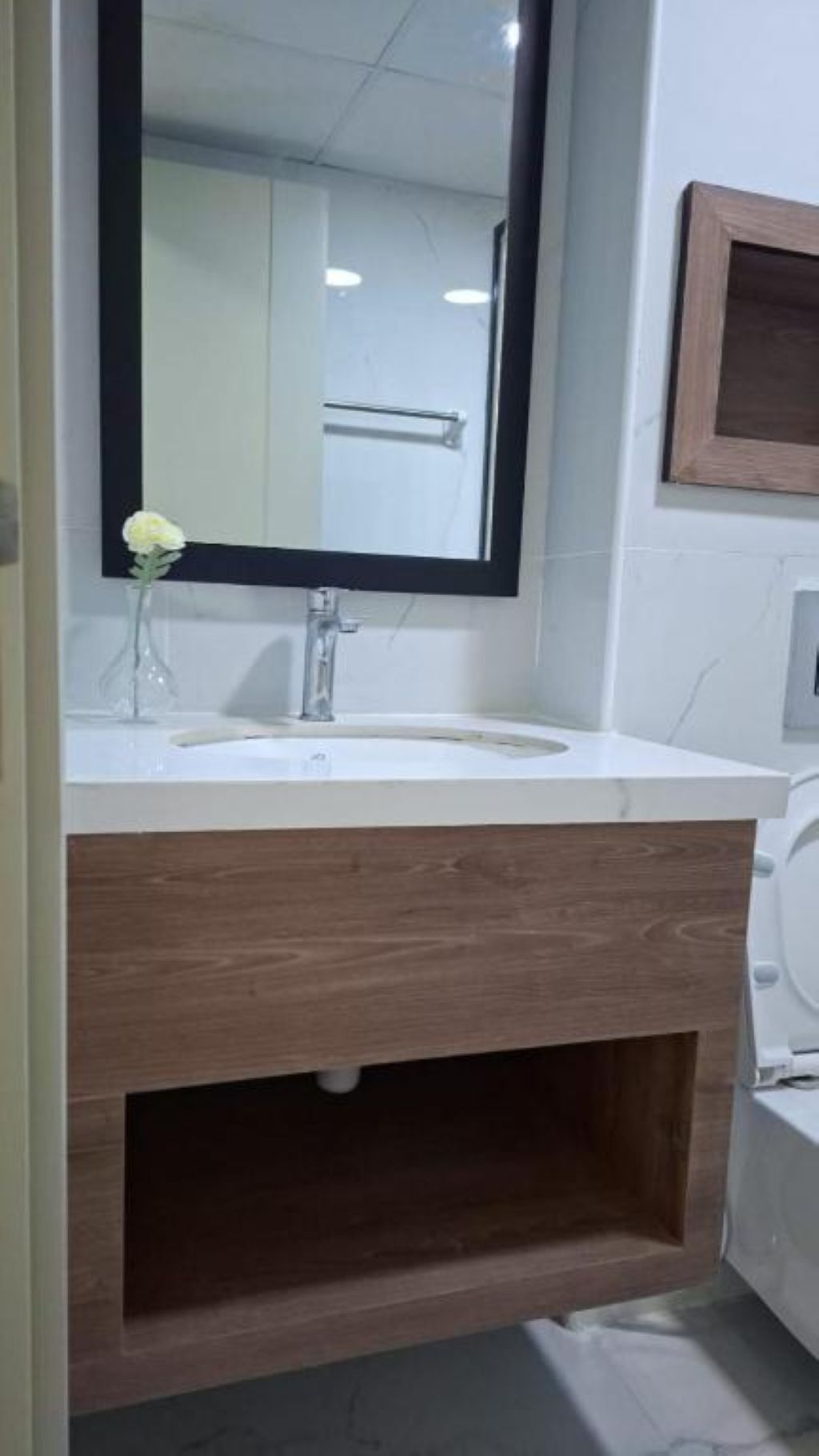 A bathroom with a white sink, a wooden vanity, and a mirror with a black frame.