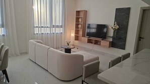 Een moderne woonkamer met een modulaire bank, een flatscreen televisie, een eettafel en een minimalistische inrichting.