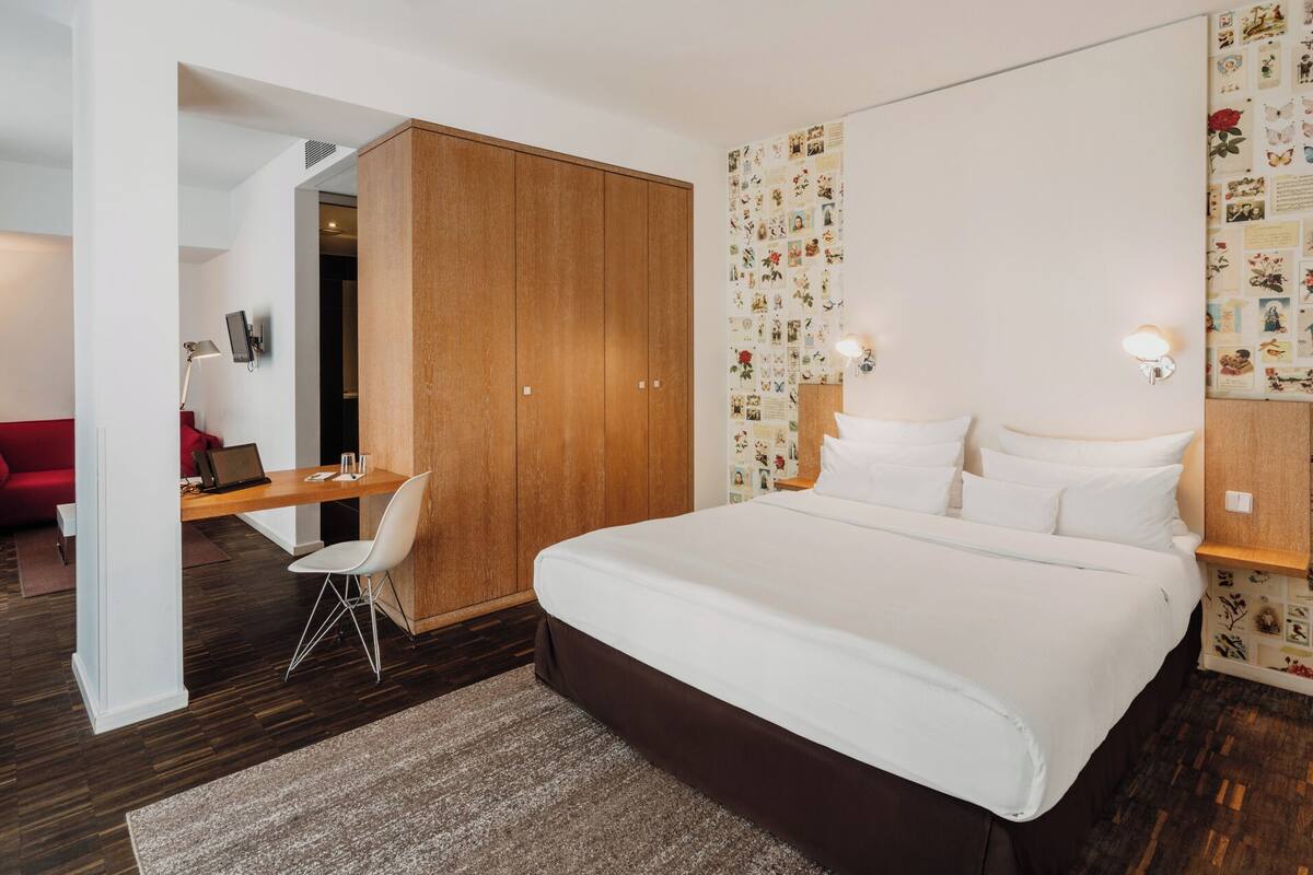 A modern hotel room with a large bed, a desk, a red sofa, and a wall decorated with vintage photos.