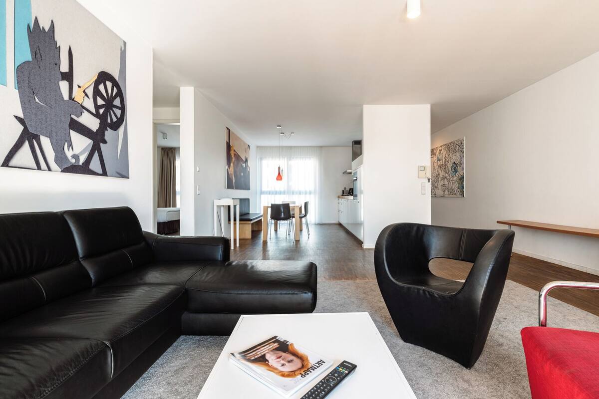 A modern living room with a black leather sofa, a red chair, and a white coffee table.