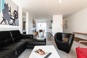 A modern living room with a black leather sofa, a red chair, and a white coffee table. - Grimms Berlin Mitte (Berlin)