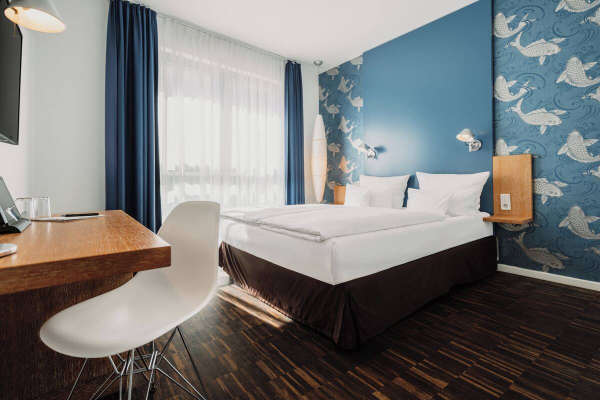 A hotel room with a bed, desk, chair, and a wall with a fish pattern.