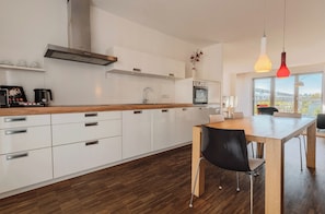 A modern kitchen with white cabinets, a wooden countertop, and a dining area with a table and chairs. - Grimms Berlin Mitte (Berlin)