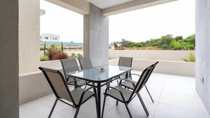 Mesa de vidrio con cuatro sillas en un balcón con vistas a zonas verdes y edificios.