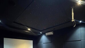 Ein Heimkinozimmer mit großer Leinwand, bequemen Sitzgelegenheiten und einer Gestaltung der Decke, die Sterne darstellt.
