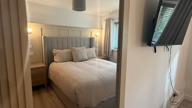Une chambre à coucher moderne, avec un lit, des tables de chevet, un téléviseur fixé au mur et un luminaire au plafond.