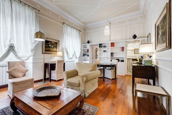 A spacious living room with a wooden coffee table, beige armchairs, and a dining area with a table and chairs. - Liberty Trastevere House (Rome)