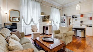 Un salón amplio con un sofá grande, una mesa de centro y una chimenea. Hay dos sillones, un televisor y una estantería.