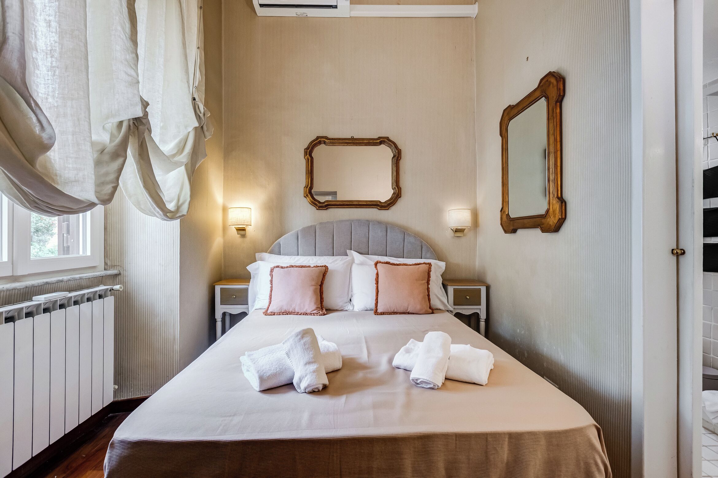 A neatly made bed with pillows and towels, a large mirror, and a radiator.