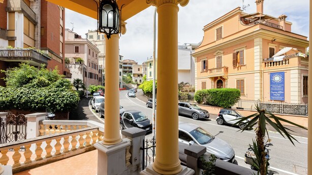 Un balcón con columnas amarillas, vista a la calle y un edificio con un letrero azul.