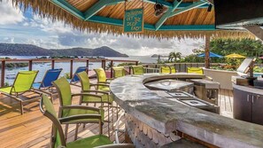 Una terraza con zona de bar, sillas y vistas al mar y a las montañas.