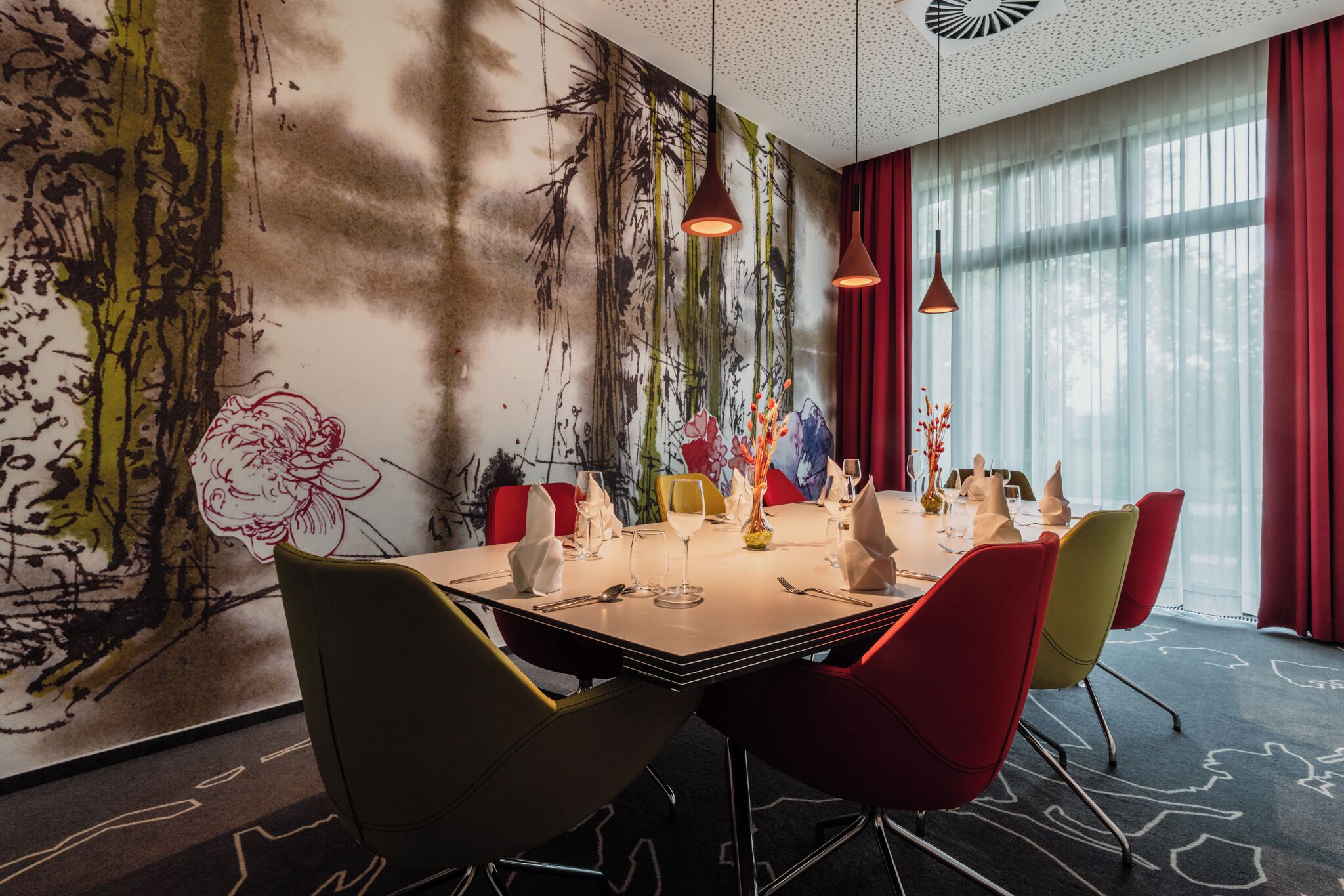 Ein Esszimmer mit einer großen Wandmalerei, einem Tisch für sechs Personen und roten und gelben Stühlen.