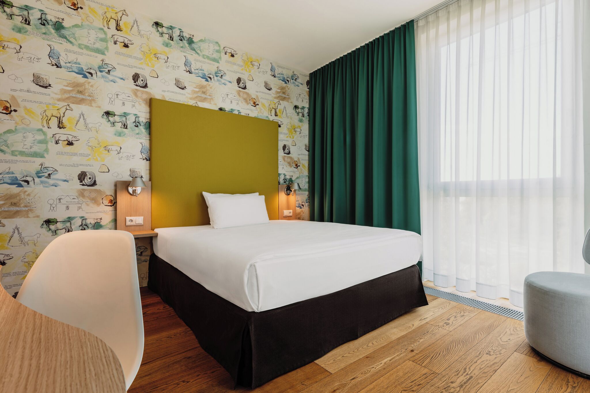 Habitación de hotel con cama, mesita de noche, lámpara, silla y ventana con cortinas.